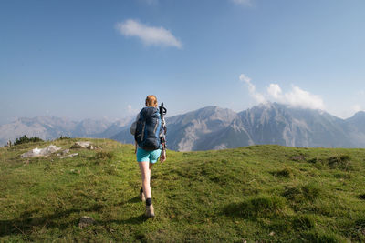 Rear view of woman hiking on mountain against blue sky