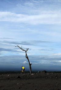 Distant view of man cycling on land against cloudy sky