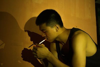 Side view of man lighting cigarette against wall