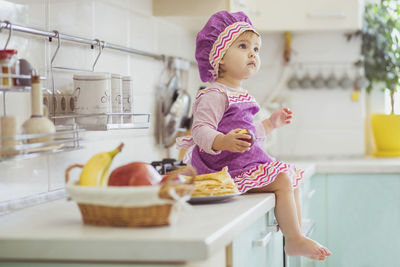 Adorable baby in an apron and chef's cap sitting with an apple on the table