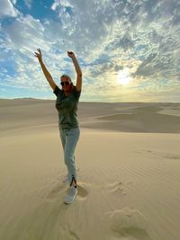 Full length of woman with arms raised standing at desert during sunset