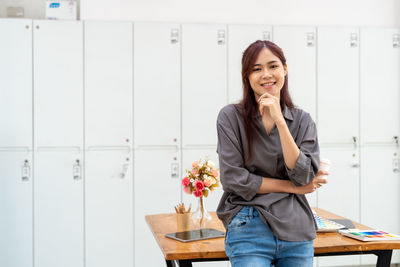 Portrait of young woman standing by table