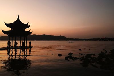 Silhouette people on lake against sky during sunset