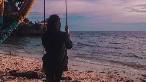 Rear view of woman standing at beach during sunset