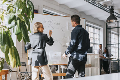 Male and female business people planning strategy over white board at office