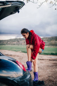 Full length portrait of woman standing by car against sky