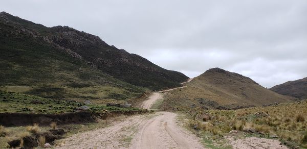 Dirt road leading towards mountains against sky