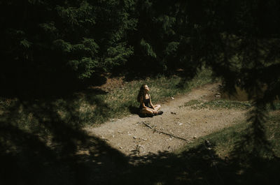 Full length of woman sitting on field amidst trees