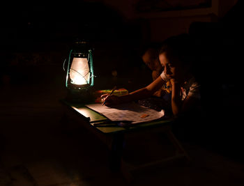 Siblings studying by illuminated lantern in darkroom