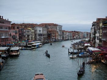 Boats moored in canal amidst buildings in city against sky