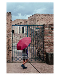 Rear view of man with umbrella against building