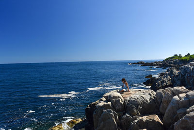 Girl sitting on rock at beach against clear sky