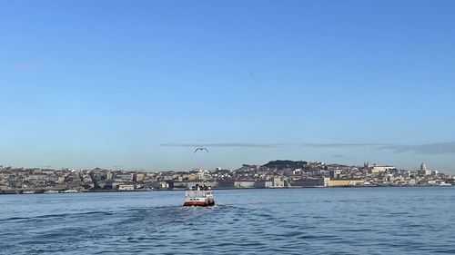 Nautical vessel on sea by buildings against clear blue sky