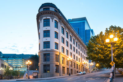 Illuminated street by buildings against sky at dusk