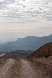 Dirt road leading towards mountains against sky