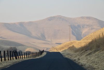 Road leading towards mountains against clear sky