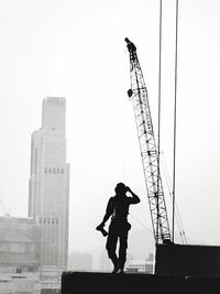 Silhouette man standing on construction site against sky with crane