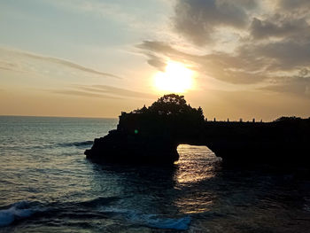 Silhouette rock in sea against sky during sunset