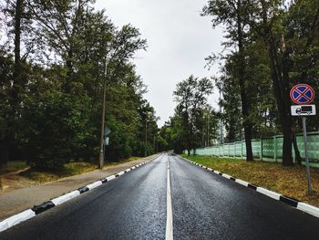 Road sign by trees against sky