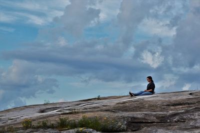 Man sitting on rock against sky