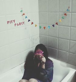 High angle view of sad young woman covering face while sitting in bathtub