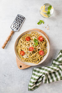 Spaghetti pasta with pesto sauce and cherry tomatoes, glass of water. top view