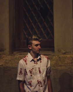 Young man standing against window at night