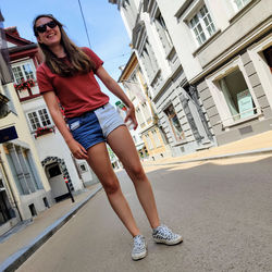 Full length of young woman wearing sunglasses standing on street in city