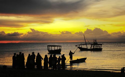 Silhouette people on beach against sky during sunset