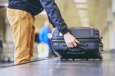 Midsection of young man taking luggage from conveyor belt at airport