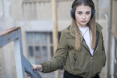 Close-up portrait of young woman listening music with hands in pocket