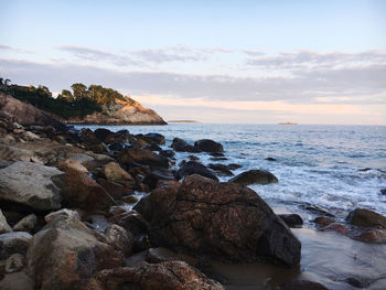 Rocks on beach against sky during sunset