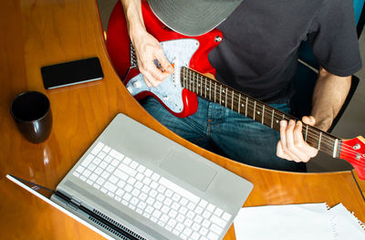 Midsection of man playing guitar at home