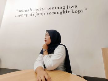 Young woman looking away while sitting on table