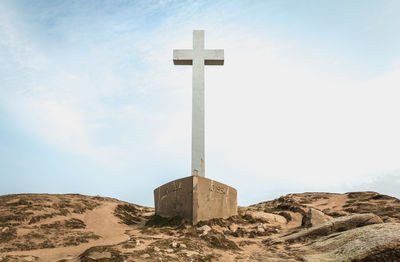 Cross on sand against sky