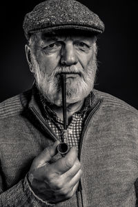 Portrait of man holding smoking pipe against black background