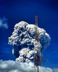 Low angle view of communications tower by smoke against blue sky