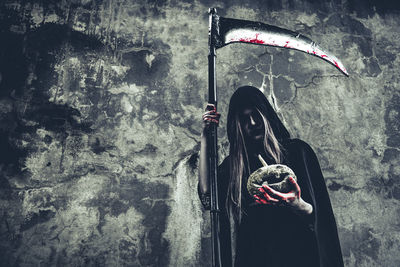 Woman holding umbrella standing against wall by building