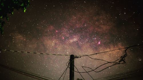 Low angle view of silhouette electricity pylon against sky at night