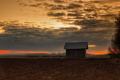 Barn on field against cloudy sky during sunset