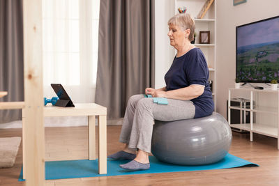 Woman exercising on fitness ball while watching tutorial on tablet at home