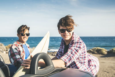 Portrait of smiling young couple sitting on sea against sky