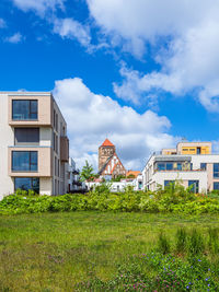 Plants growing on field by buildings against sky