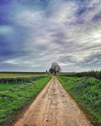 Dirt road amidst field against sky