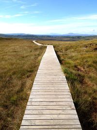 Boardwalk leading towards landscape against sky