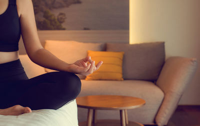 Midsection of woman meditating while sitting on bed at home