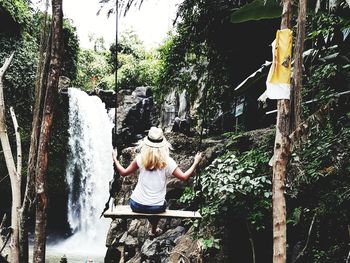 Rear view of woman looking at waterfall in forest