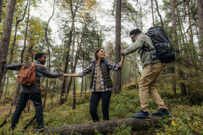 Happy woman helping man and son while walking on log in forest