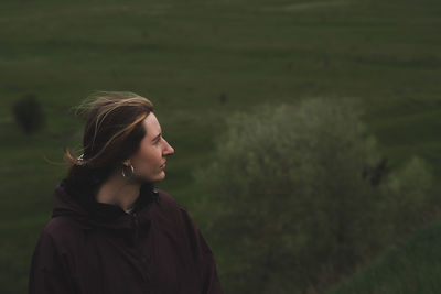 Woman in a rain anorak stands on the hill, deep green background. 