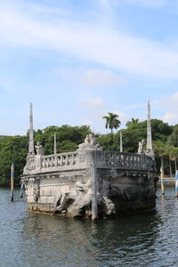 Built structure on riverbank against cloudy sky